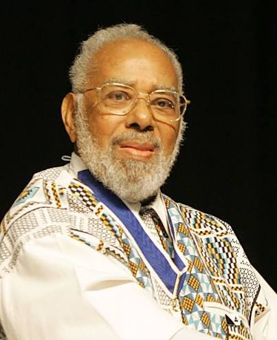 Retrato fotográfico de Abdias Nascimento, de cabelos e barba grisalhos, óculos e túnica com padrões africanos.