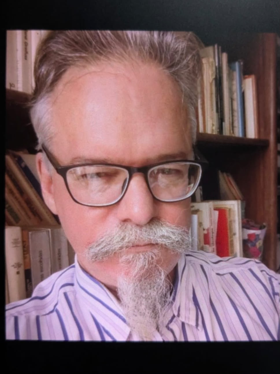 Retrato oficial de Políbio Campos, homem de cabelos grisalhos, óculos de armação escura, bigode e cavanhaque grisalhos, usando camisa listrada em azul e branco, diante de uma estante de livros.