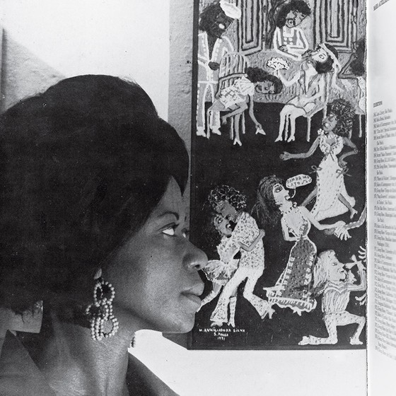 Retrato fotográfico em preto e branco de Maria Auxiliadora de perfil diante de uma de suas pinturas.