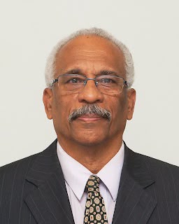 Retrato oficial de Antonio Alberto Lopes, homem de cabelos grisalhos, óculos, bigode, terno escuro listrado, camisa rosa claro e gravata estampada, sobre fundo neutro claro.