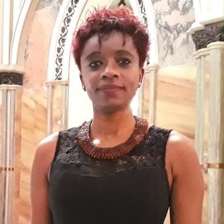 Retrato oficial de Rosa Maria dos Santos, sorrindo, com cabelo curto ruivo, colar de contas douradas e vestido preto com renda, em ambiente interno com colunas claras ao fundo.